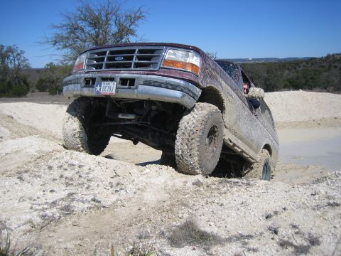 1996 Ford Bronco - This truck is navigating a challenging off-road terrain with muddy tires and suspension.
