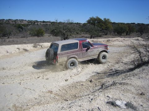 1996 Ford Bronco - A red 1996 Ford Bronco kicks up mud as it drives off-road on a sunny day.