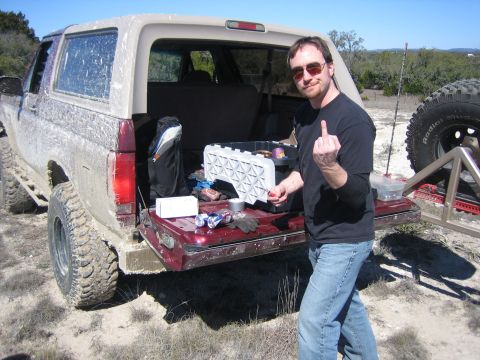 1996 Ford Bronco - A man stands by the open tailgate of a dirty Ford Bronco, gesturing with his middle finger.