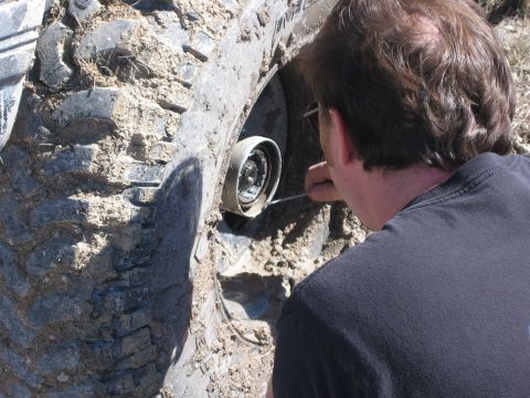 1996 Ford Bronco - A person is focused on the hub of a heavily mud-caked tire, suggesting off-road use.