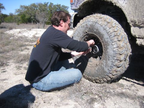 1996 Ford Bronco - A man kneels to adjust the hub on a heavily mud-caked off-road vehicle tire.