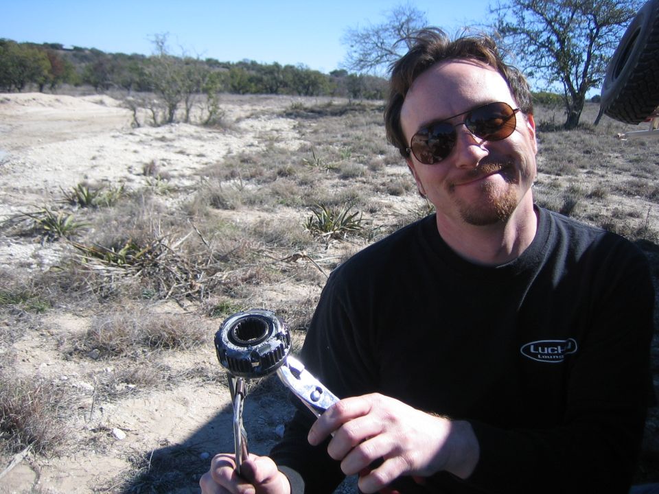 Man holds a vehicle part, possibly a hub assembly, in a dry, outdoor environment