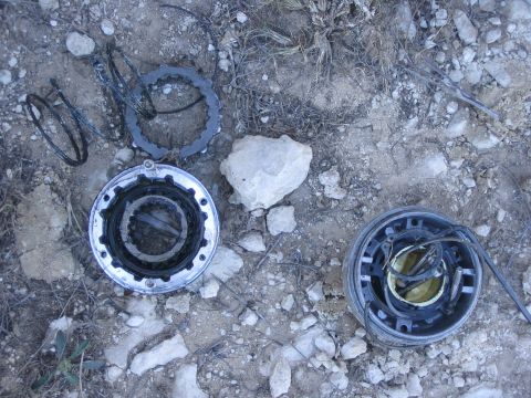 1996 Ford Bronco - Vehicle parts, possibly from a hub or transmission, lie on the ground next to a rock.