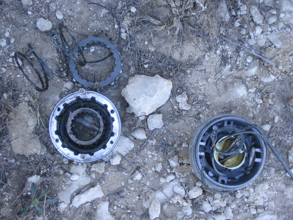 Disassembled vehicle parts, including gears and springs, scattered on rocky ground