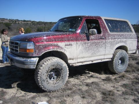 1996 Ford Bronco - A heavily mud-covered Ford Bronco is shown in a dry, outdoor environment.