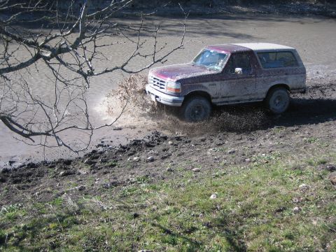 1996 Ford Bronco - A Ford Bronco navigates a muddy, watery terrain, creating a large splash.