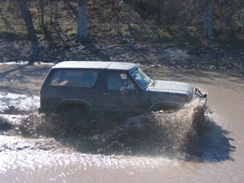 1996 Ford Bronco - This 1996 Ford Bronco is navigating a muddy off-road trail, splashing water as it goes.