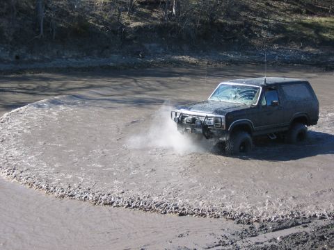 1996 Ford Bronco - A black Ford Bronco navigates a muddy terrain, kicking up a significant amount of spray.