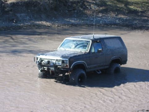 1996 Ford Bronco - This black Ford Bronco, likely from the 1987 model year, navigates through a muddy terrain.