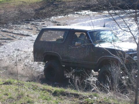 1996 Ford Bronco - An SUV navigates a challenging muddy terrain, kicking up dirt and water as it goes.