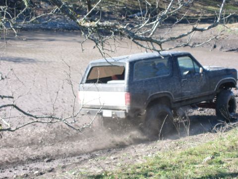 1996 Ford Bronco - A lifted Ford Bronco kicks up mud as it drives through a muddy terrain.