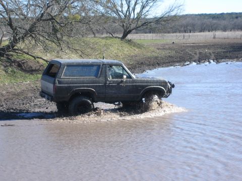1996 Ford Bronco - This dark SUV navigates through a muddy water crossing, appearing to be from the 1987 model year.