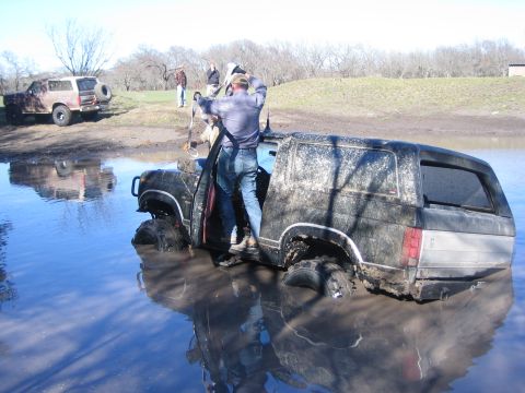 1996 Ford Bronco - A 1996 Ford Bronco is stuck in the mud, with several people nearby, one attempting to get out.