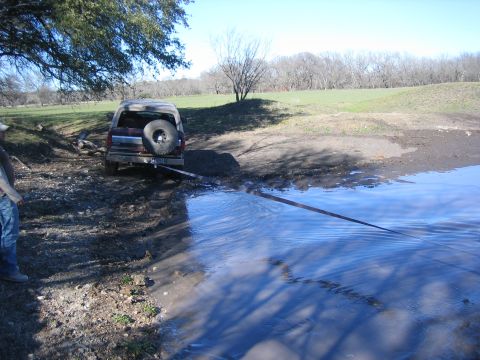 1996 Ford Bronco - Ford Bronco stuck in mud near a body of water with a strap attached.