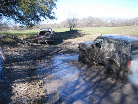 1996 Ford Bronco - Two off-road vehicles are struggling to get through a muddy terrain, with one vehicle in the foreground and another in the background.