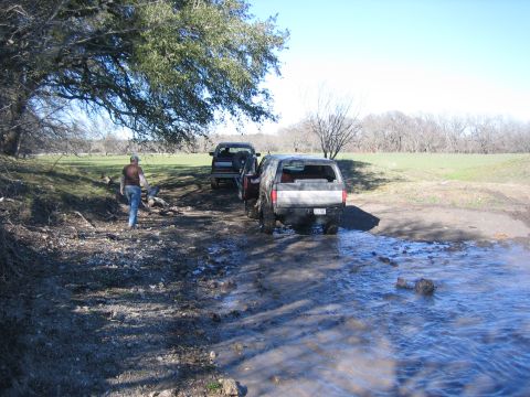 1996 Ford Bronco - Two SUVs navigate a challenging, wet terrain with a person walking ahead.
