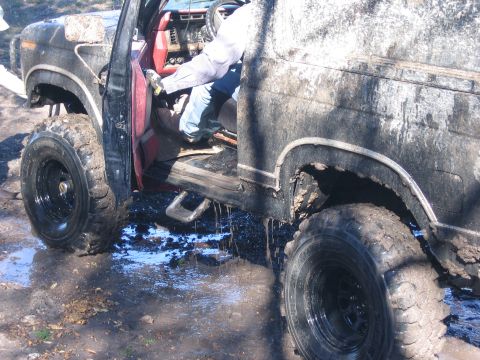 1996 Ford Bronco - A mud-covered 1996 Ford Bronco is shown with its door open, revealing the red interior and a person entering.