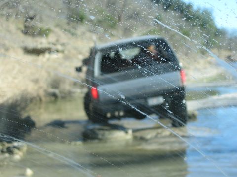 1996 Ford Bronco - A dark SUV navigates through a shallow body of water, seen from behind.