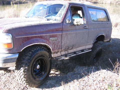 1996 Ford Bronco - Muddy 1996 Ford Bronco navigating rough terrain with large off-road tires.
