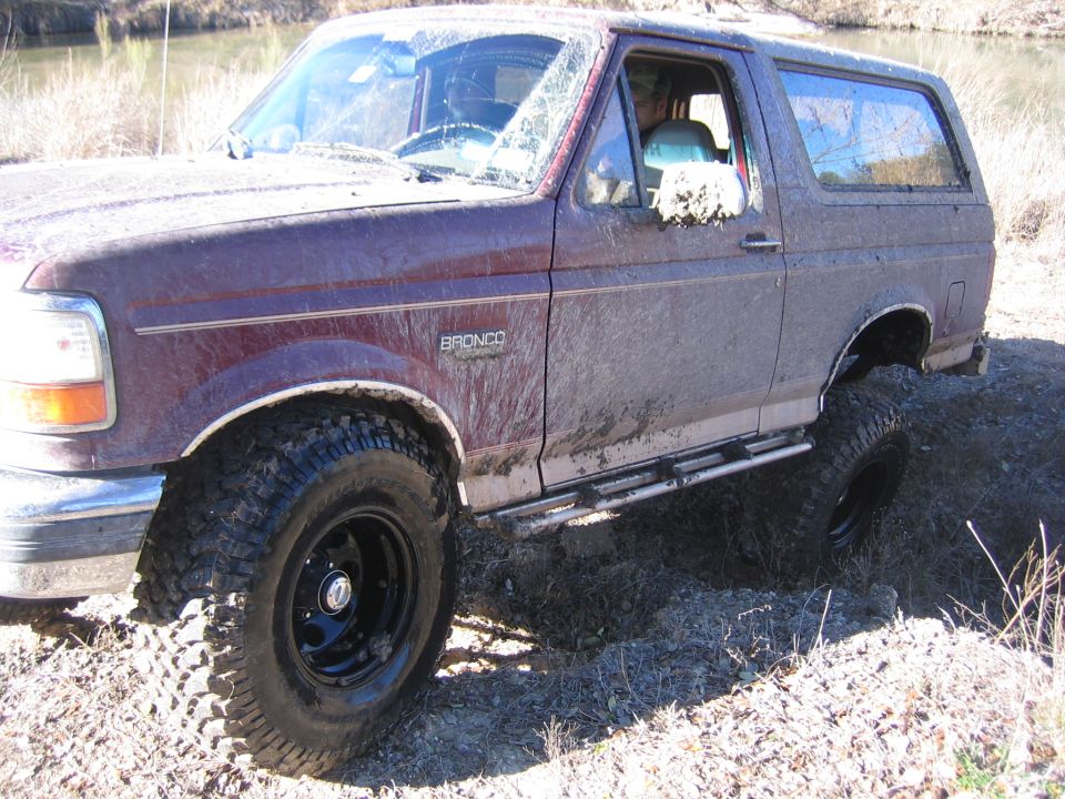 Mud-covered 1996 Ford Bronco with aftermarket side steps, driving off-road