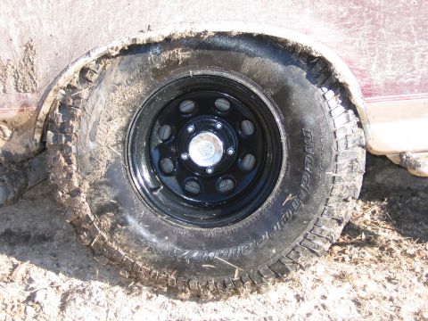 1996 Ford Bronco - A close-up of a muddy tire and fender on a maroon vehicle.