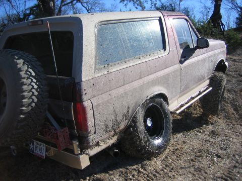 1996 Ford Bronco - Mud-covered 1996 Ford Bronco parked off-road with a spare tire on the back.