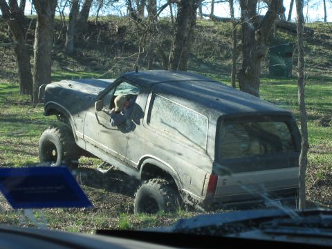 1996 Ford Bronco - This 1996 Ford Bronco is navigating a muddy, wooded terrain with a driver visible.
