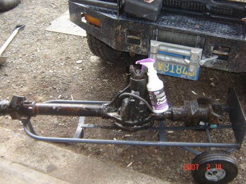 1993 Ford Bronco - A rear axle assembly is shown on a stand, with a bottle of cleaner nearby. Part of a truck with a winch is visible in the background.