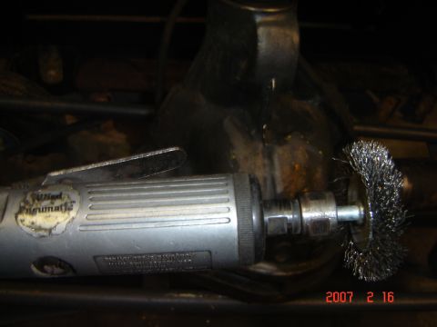 1993 Ford Bronco - An air grinder with a wire wheel is being used to clean a metal component.