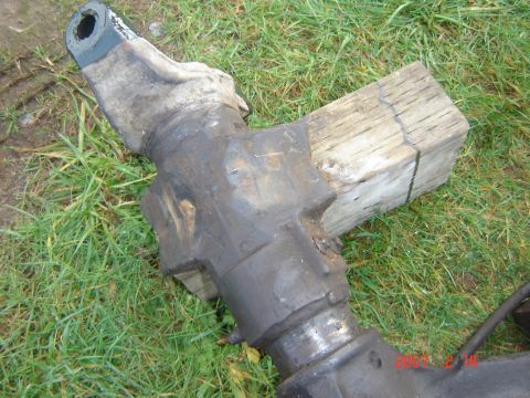 1993 Ford Bronco - A close-up view of a heavy machinery component, likely an axle, situated outdoors on grass and a wooden block.