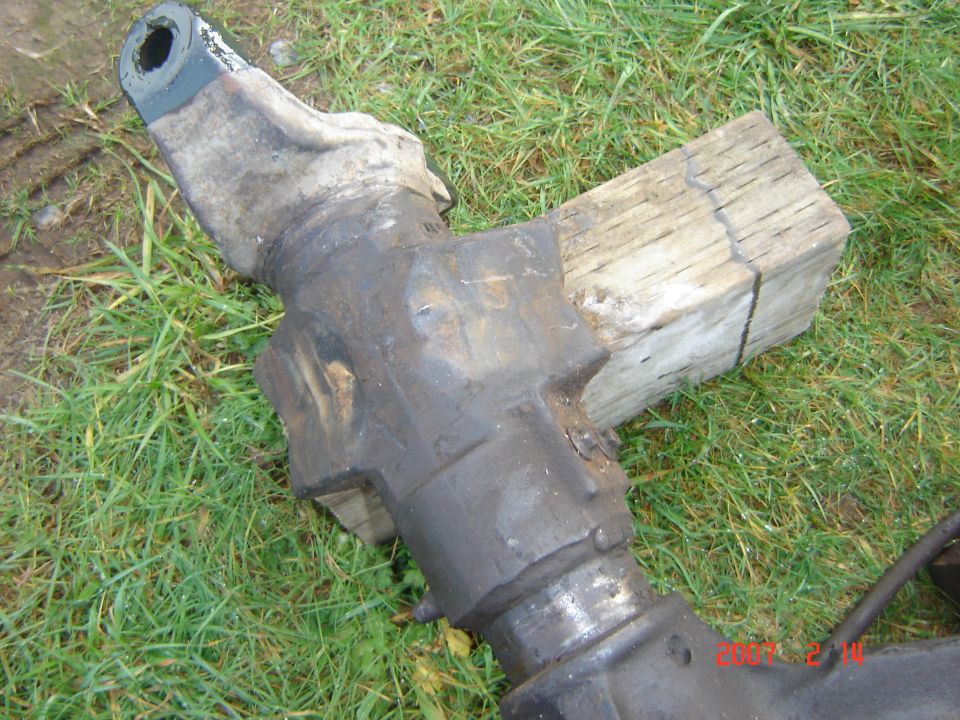 Heavy machinery part, possibly axle, resting on wood and grass
