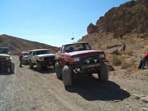 1988 Ford Bronco - Several off-road vehicles are parked on a dirt road in a desert landscape.