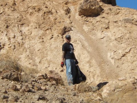 1988 Ford Bronco - A person stands on a dry, rocky slope, holding a black trash bag, likely after a cleanup effort.