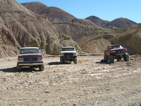 1988 Ford Bronco - Three trucks are parked in a rocky, desert landscape with hills in the background.