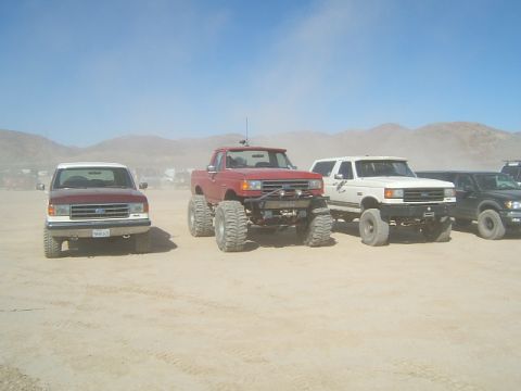 1988 Ford Bronco - A white Ford Bronco is parked in a dusty lot with other lifted trucks and SUVs.