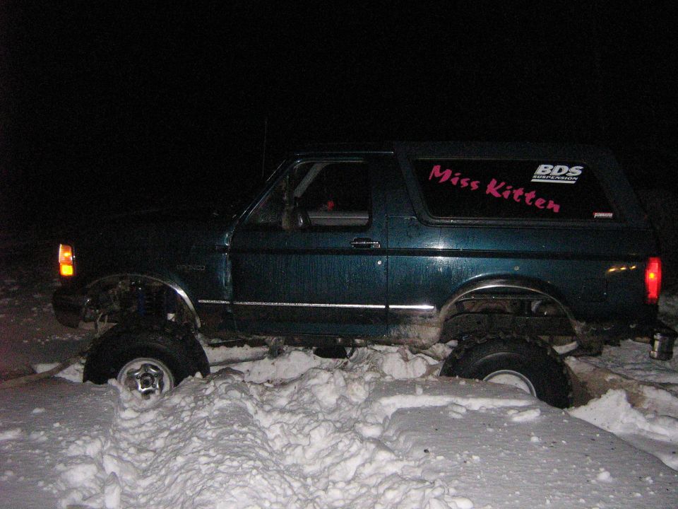Green Ford Bronco stuck in snow, side view. Lifted suspension, "Miss Kitten" sticker on rear window