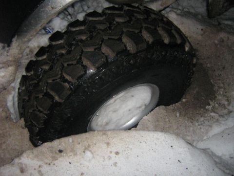 1995 Ford Bronco - A vehicle's tire is deeply embedded in snow, highlighting its tread and a portion of the silver rim.