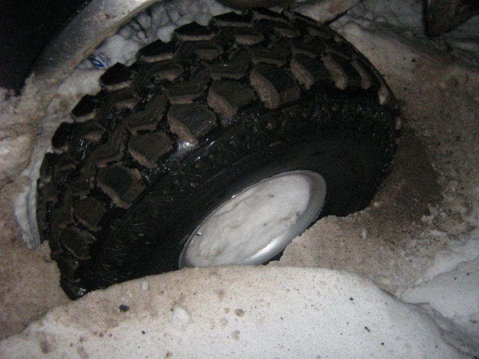 Tire stuck in snow, showing aggressive tread pattern and silver rim