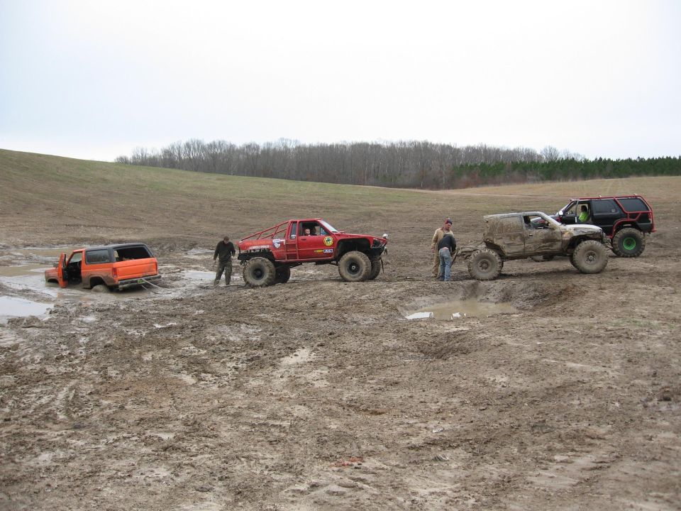 Orange SUV stuck in mud, door open, being towed by a red truck