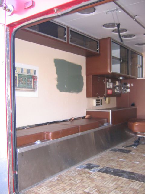1984 Ford F-350 - The interior of a vehicle, possibly an ambulance or camper, is shown with brown seating and cabinetry, and a patch of green paint on the wa…
