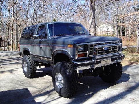 1986 Ford Bronco - A lifted two-door Ford Bronco SUV in dark gray/black with a chrome grille and 'Ford' lettering, shown from the front three-quarter angle on…