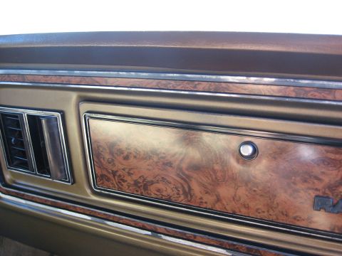 1979 Ford Bronco - The dashboard features faux woodgrain paneling and chrome accents around the air vents and a lockable compartment.