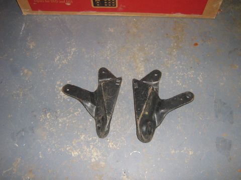 1995 Ford Bronco - Two vehicle suspension brackets are shown on a concrete floor with a cardboard box in the background.