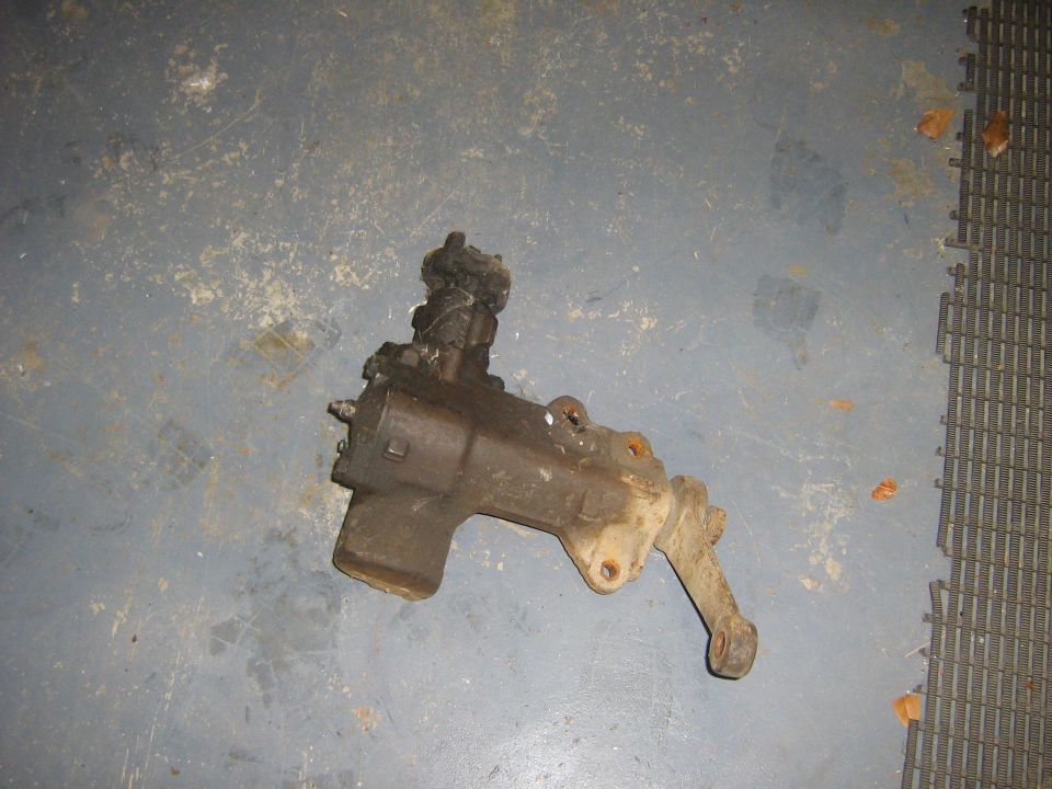 Steering gear box with pitman arm attached, resting on a grey floor