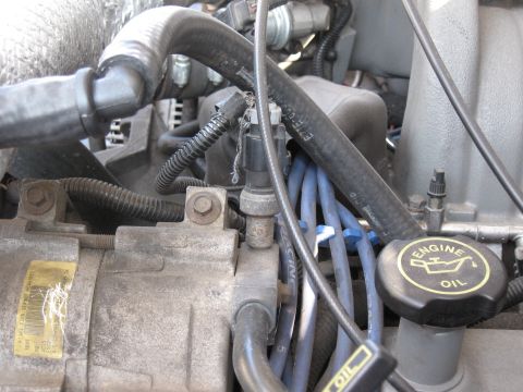1994 Ford Bronco - Tight engine-bay detail showing the A/C compressor with its yellow Ford refrigerant charge label, the black screw-on 'ENGINE OIL' filler ca…