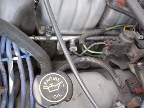 1994 Ford Bronco - Close-up of an engine bay, focusing on the black engine oil cap with its distinctive yellow text and graphic.