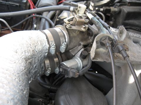 1994 Ford Bronco - Engine-bay close-up of a throttle body fed by an intake tube wrapped in reflective foil/bubble heat-shield insulation and secured with doub…