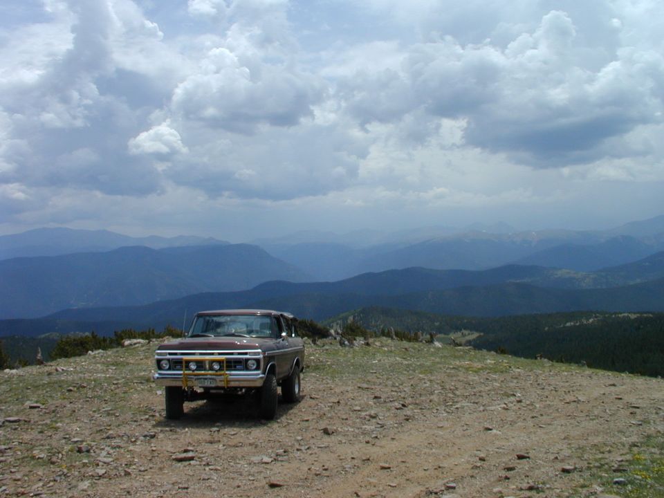 Lifted maroon Ford 4x4 parked on gravel mountain ridge under storm clouds
