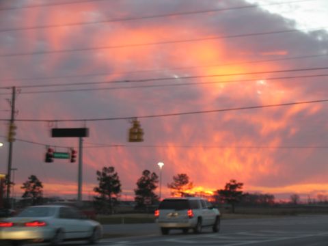 1978 Ford Bronco - A vibrant sunset paints the sky with fiery colors over a road intersection with traffic.