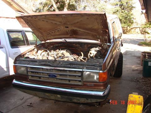 1987 Ford Bronco - This 1987 Ford Bronco has its hood open, revealing the engine compartment. A white truck is parked nearby.